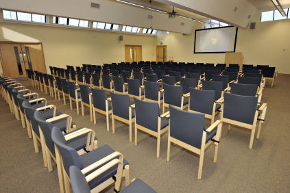 Chairs lined up inside a large room facing a smartboard on the wall at the far end