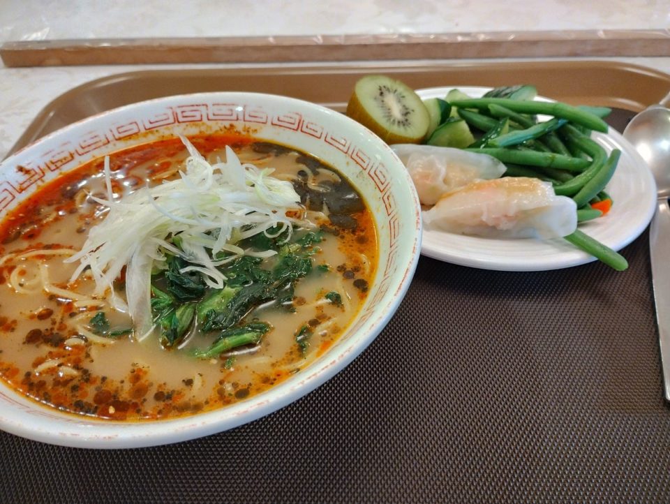 A bowl of soup and a plate of fish steaks and green beans on a table