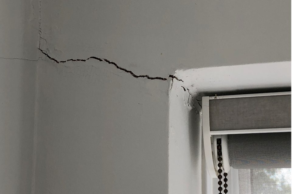 A large crack runs across a white wall to the corner of a window.